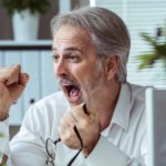 A man clenches his fists with glee having seen the share price go up on the computer screen in front of him.