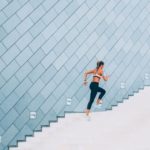 A female runner climbs a set of stairs, running with strength and pace.