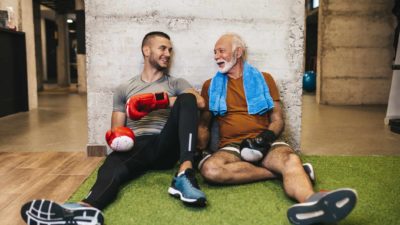 A older man and younger man rest, exhausted but happy after a good boxing session.