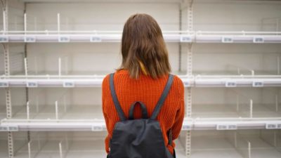 A woman stands facing a set of shelves that is completely empty.