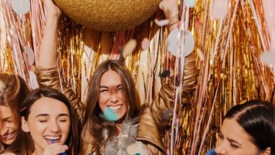 Girls at a party are surrounded by gold streamers, a golden ball and are having a fun time.
