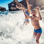 Two kids play joyfully in the crashing waves.
