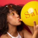 A woman inflates a balloon with the word 'sale' on it.