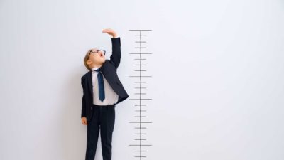 A kid stretches up to reach the top of the ruler drawn on the wall behind.