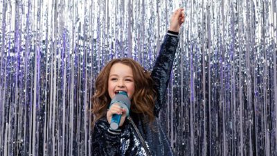 A little girls sings her heart out on stage with tinsel sparkling behind her, she is a star.