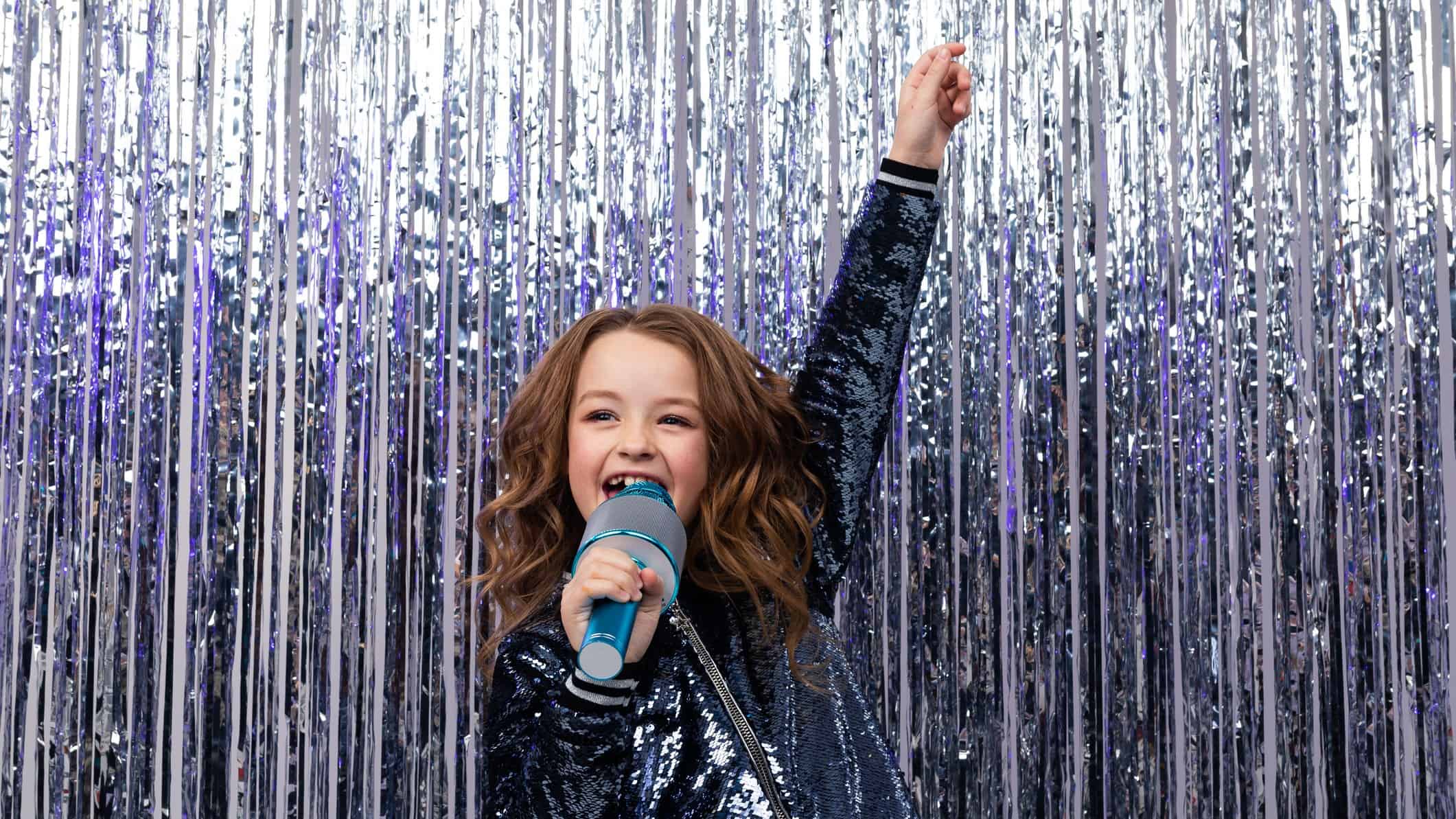 A little girls sings her heart out on stage with tinsel sparkling behind her, she is a star.