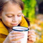 A little girl brings her mug of hot milk close to her mouth, ready to take a big sip.