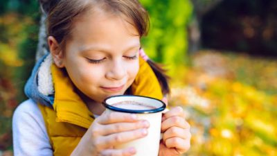 A little girl brings her mug of hot milk close to her mouth, ready to take a big sip.