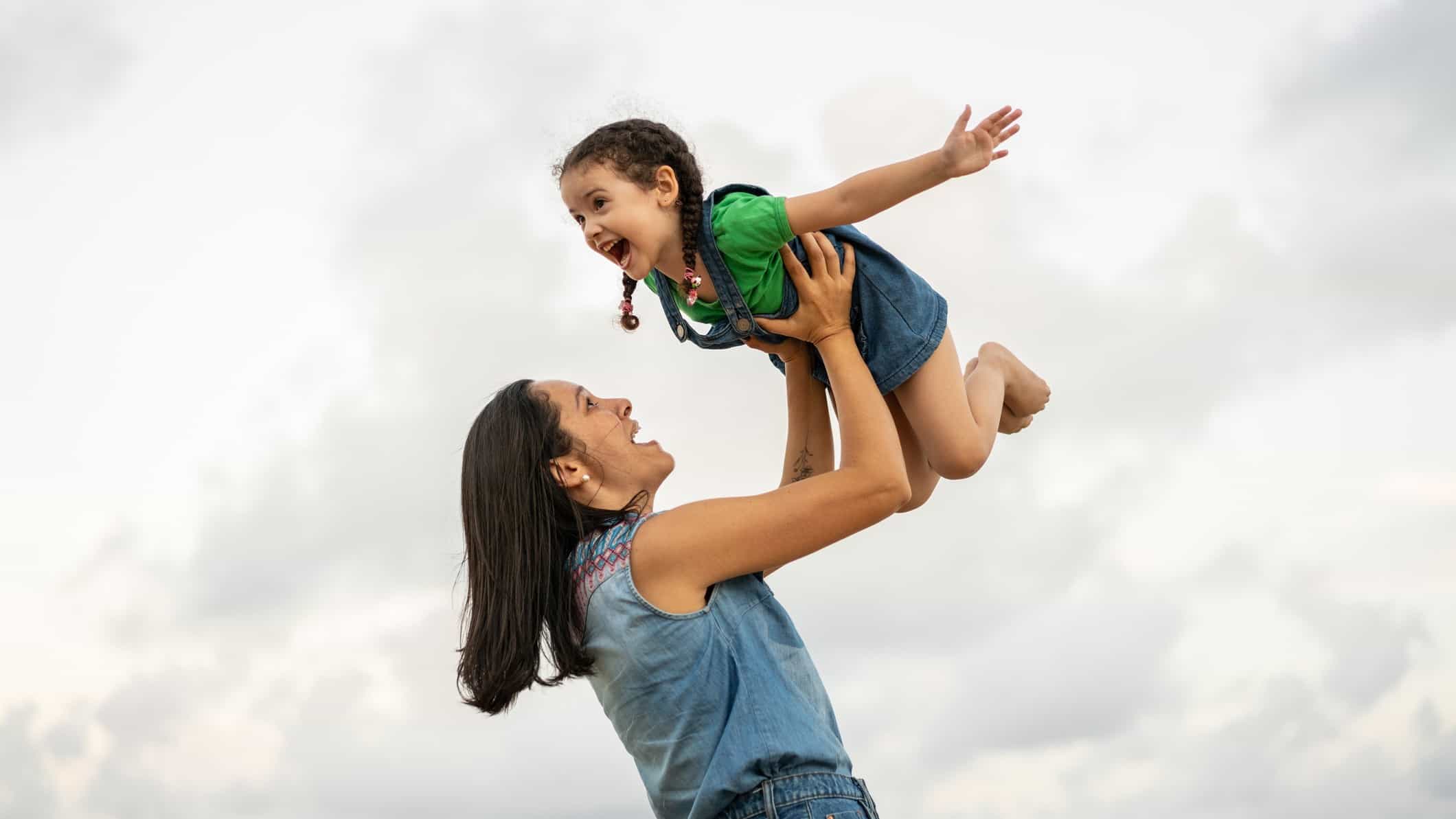 A mum lifts her daughter high into the air so she can fly.