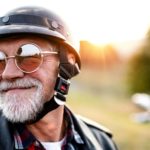 An older man wearing a helmet is set to ride his motorbike into the sunset, making the most of his retirement.