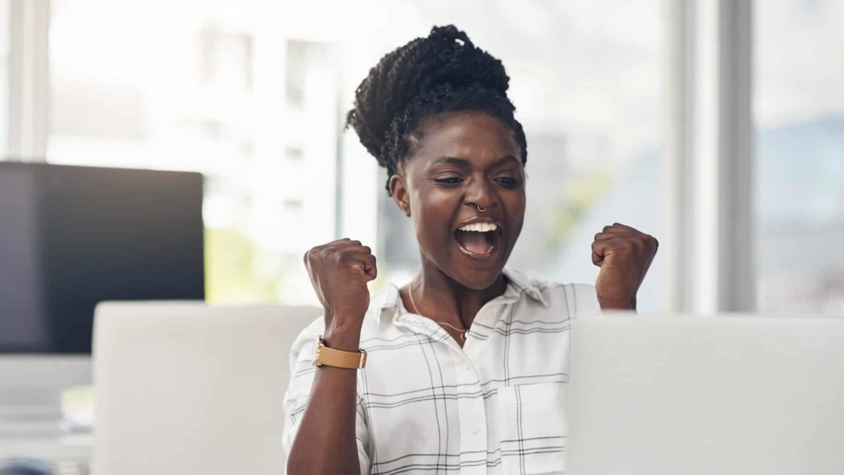 A women cheers with clenched fists having read some good news on her laptop.