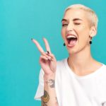 A tattoed woman holds two fingers up in a peace sign.