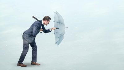 A person holds strong behind their umbrella as they weather the oncoming storm.