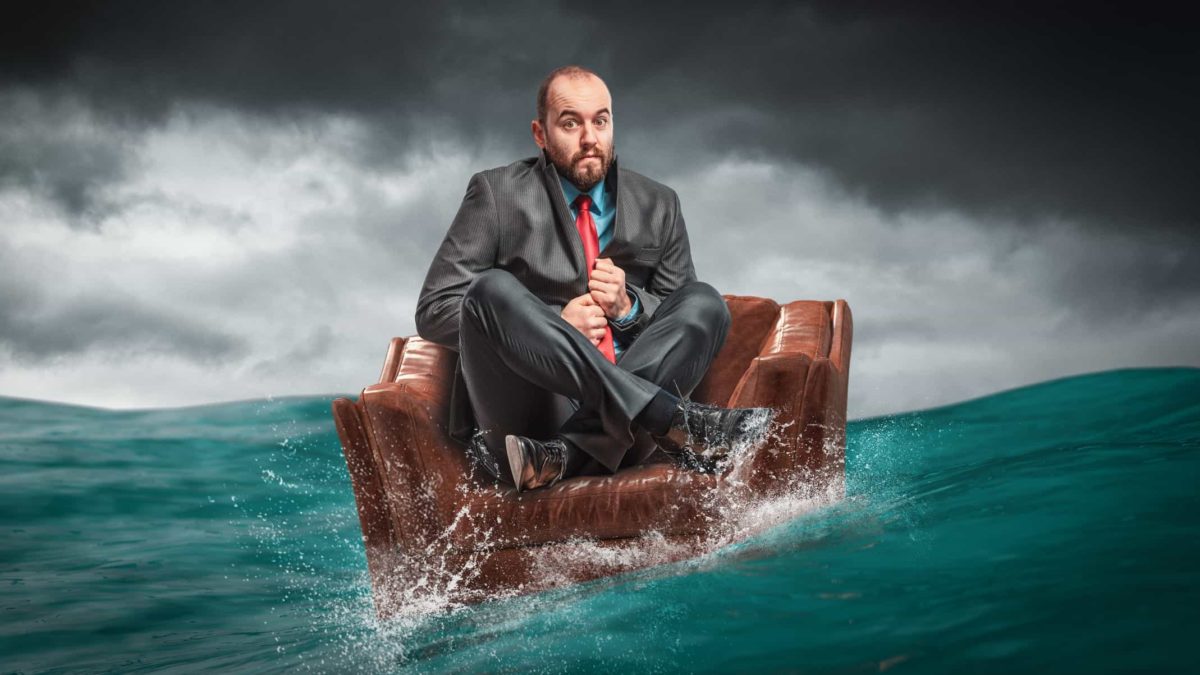 A businessman sits on an armchair adrift at sea representing the Evolution share price being in choppy waters of late