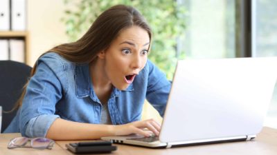 Woman looks amazed and shocked as she looks at her laptop.
