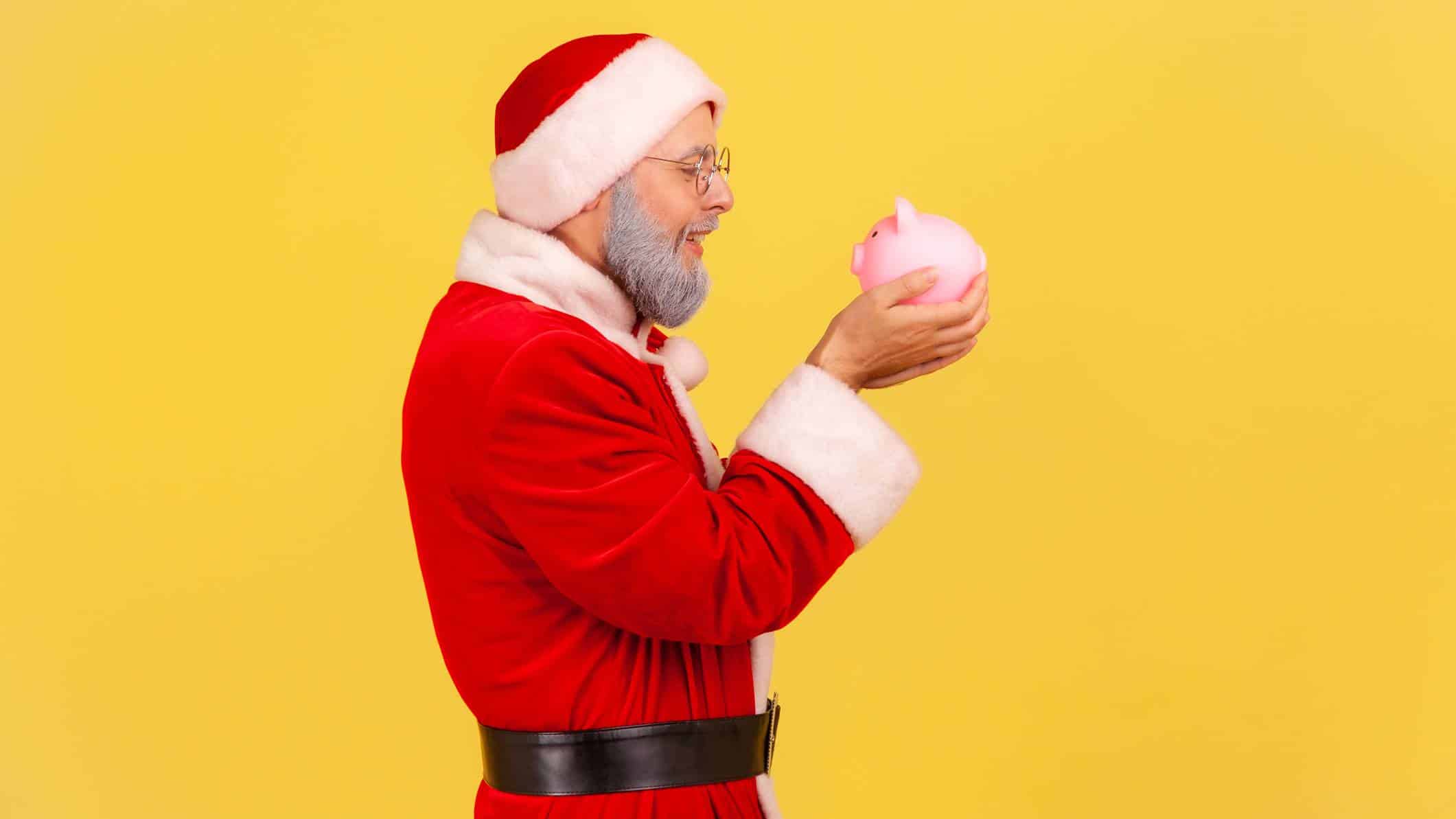 man dressed as santa holding a piggy bank