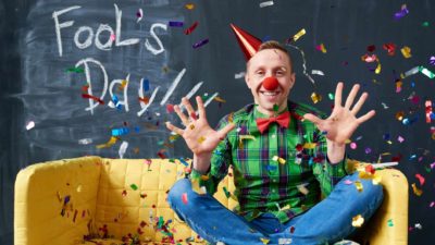 man wearing a clown hat in front of a board that says Fool's Day