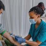 a nurse wearing a medical mask prepares a patient for a blood donation in a surgical setting.