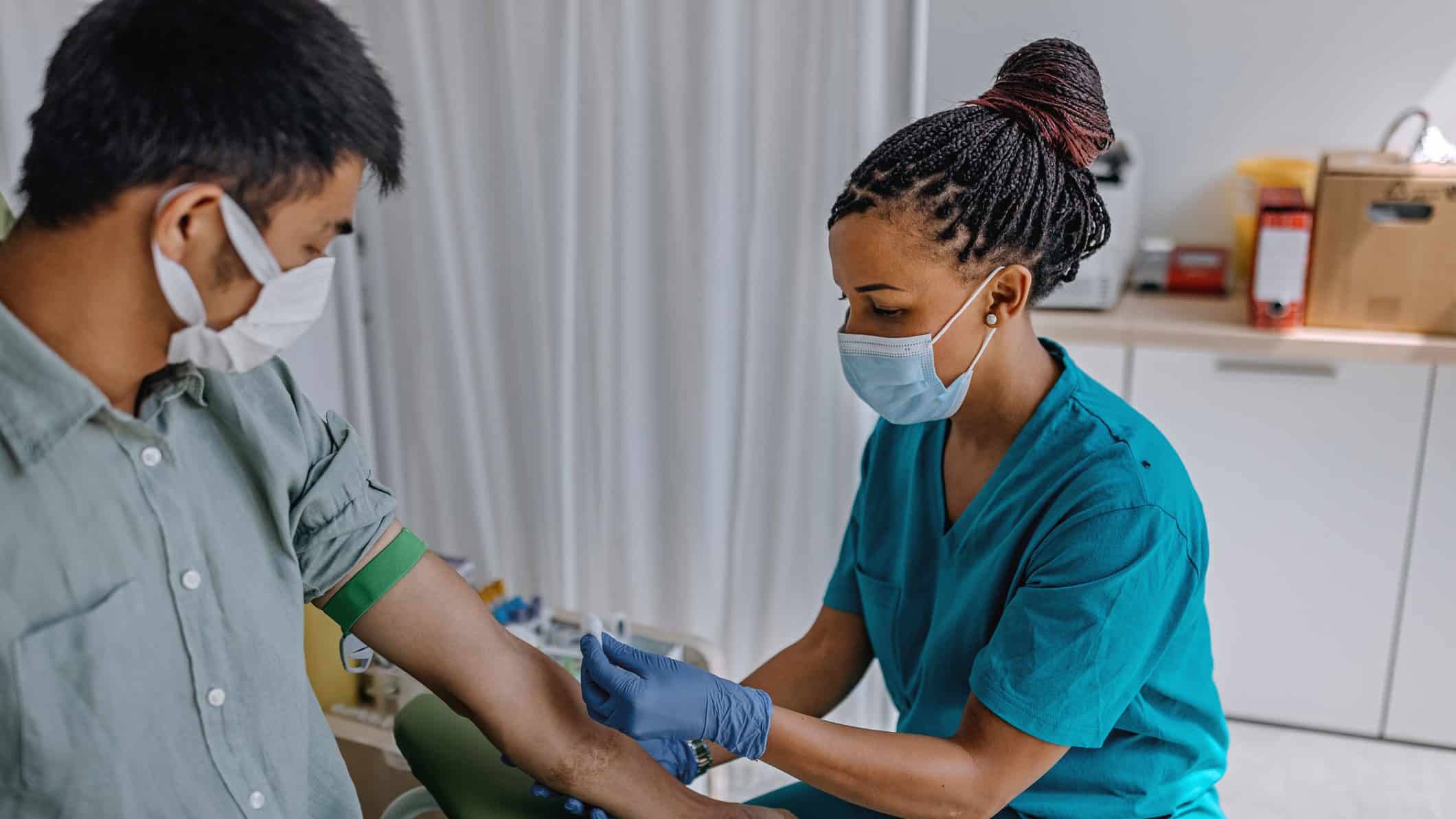 a nurse wearing a medical mask prepares a patient for a blood donation in a surgical setting.