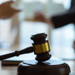 A gavel on the table at court as hands gesticulate behind it.