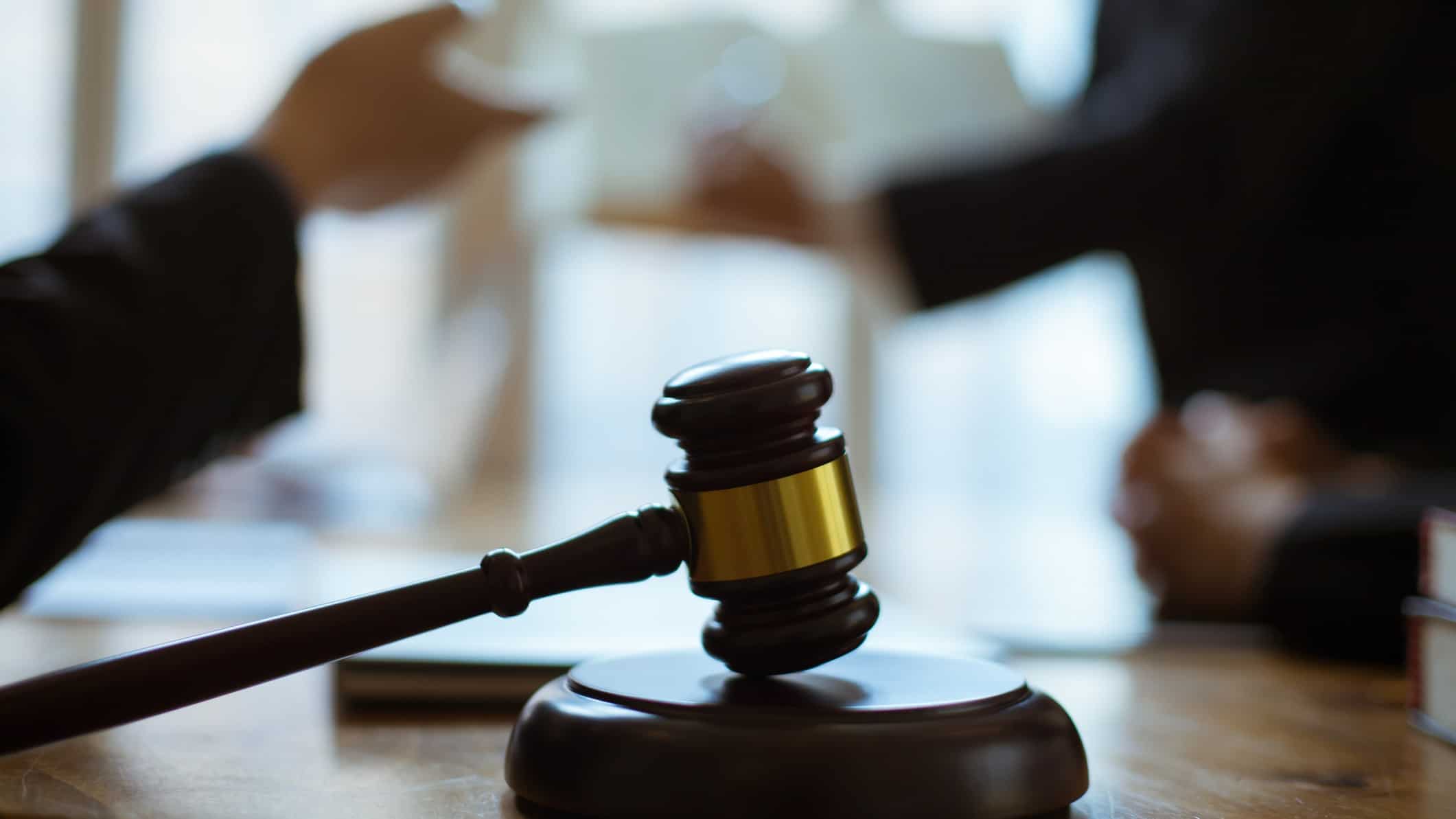 A gavel on the table at court as hands gesticulate behind it.