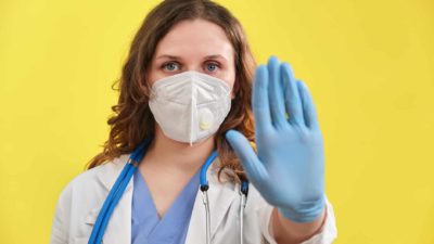 Female doctor with a mask holds out hand in a stop gesture.