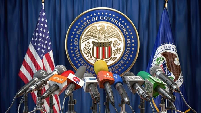 a picture of the US federal reserve podium for making media announcements complete with US flag and federal reserve flag in the background and a large array of microphones set up.