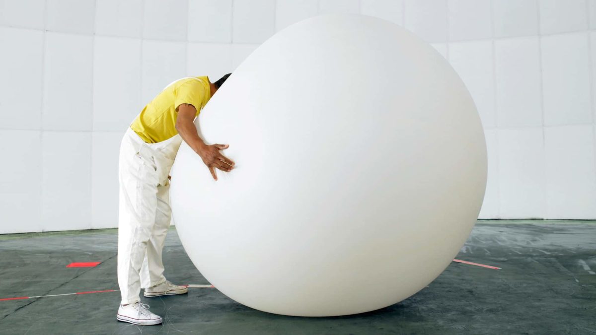 A person sinks their face into a large, round, white inflatable ball.