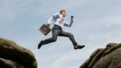 A businessman jumps outdoors in sky between two rocks.