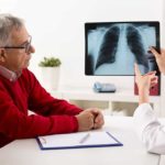 A doctor and an elderly couple sit at a desk and look at a lung scan uploaded.