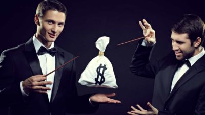 two magicians wearing dinner suits with bow ties wave their magic wands over a levitating bag with a dollars sign on it.