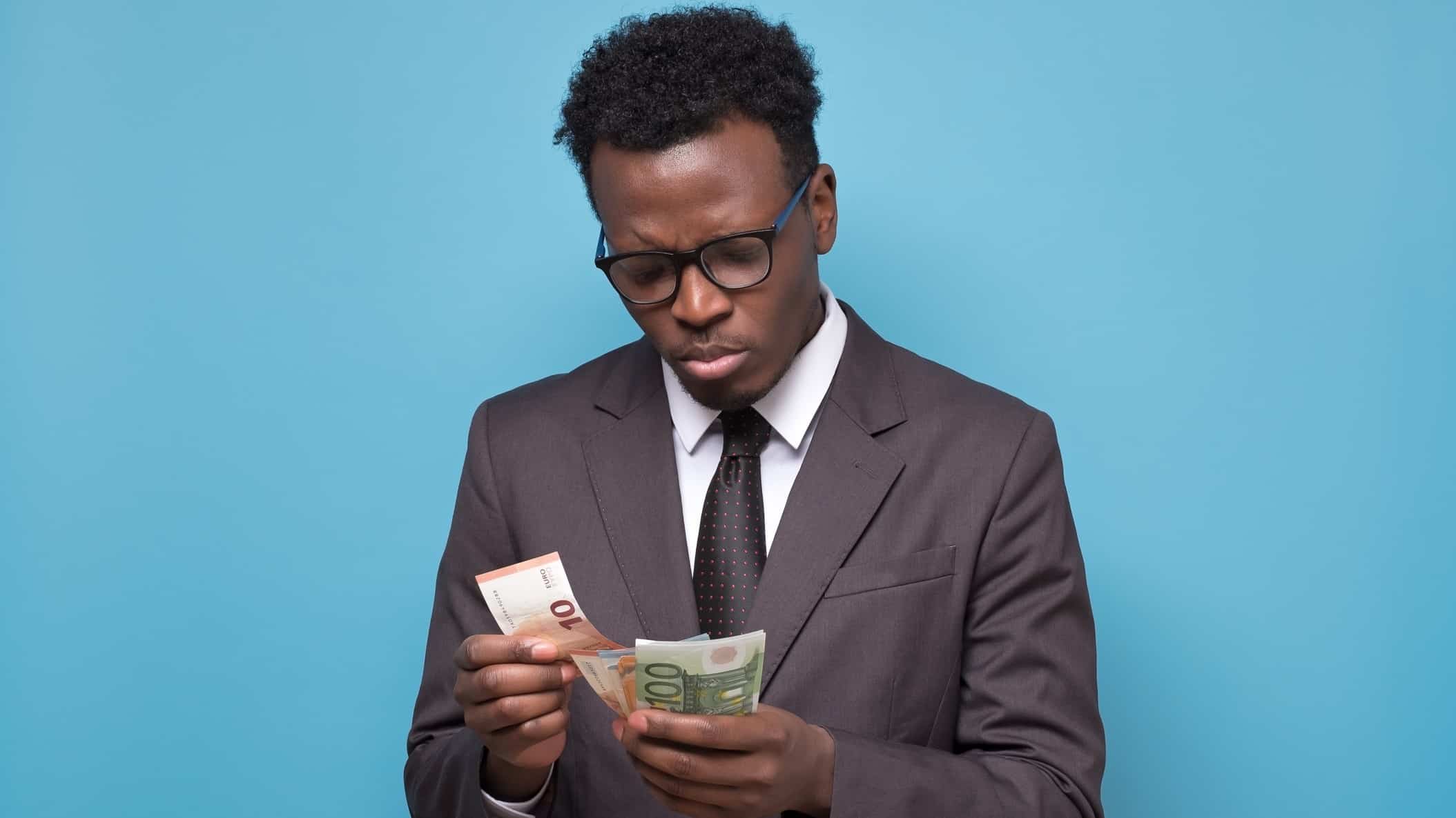a man in a snappy business suit looks disappointed as he counts bank notes in his hand.