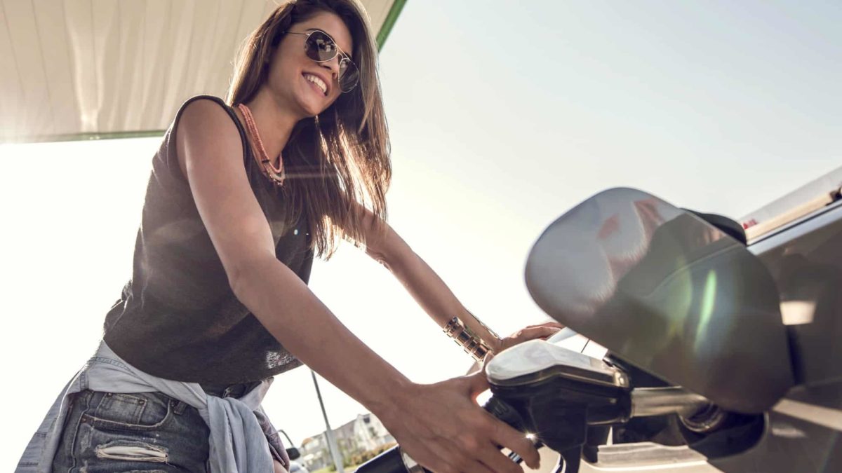 A smiling woman puts fuel into her car at a petrol pump.