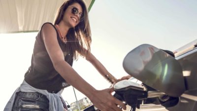 A smiling woman puts fuel into her car at a petrol pump.