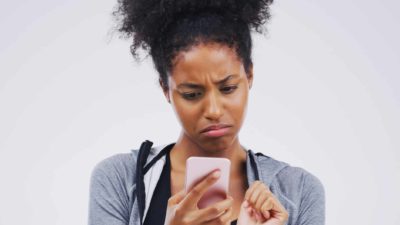 A woman with a sad face looks to be receiving bad news on her phone as she holds it in her hands and looks down at it.