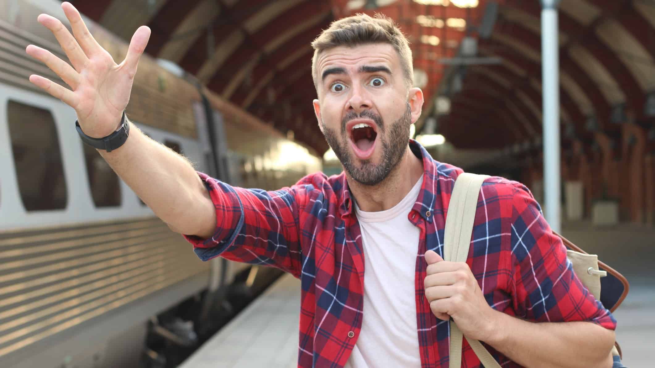 A man holds his hand out and yells for a train to wait for him on a train platform with the train in the background.