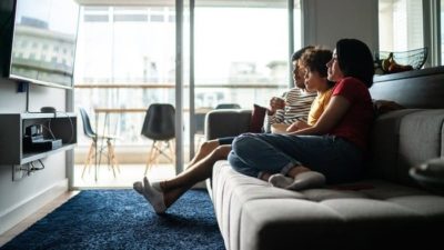 a family sits together on their sofa watching television.