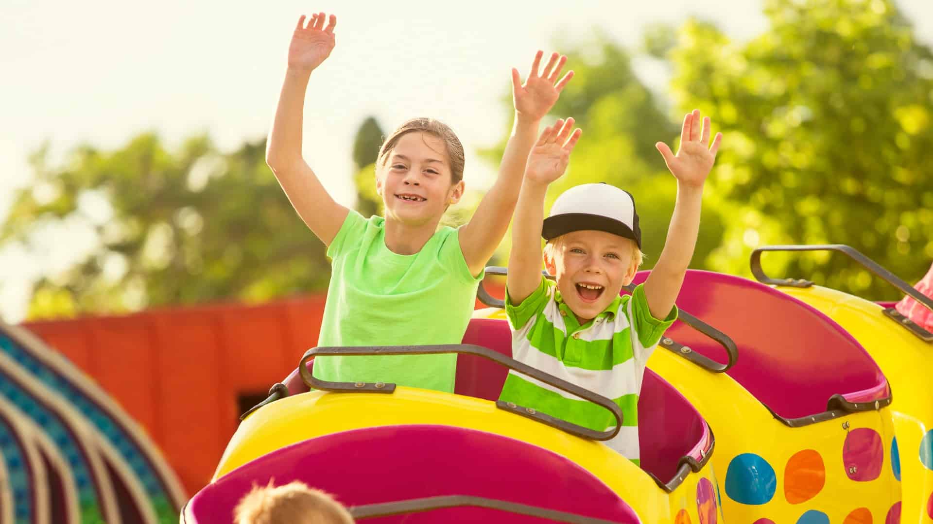 Two children put their hands in the air on a rollercoaster ride.