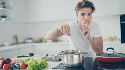 Man cooking and telling to be quiet with his finger on his lips, symbolising a secret sauce.