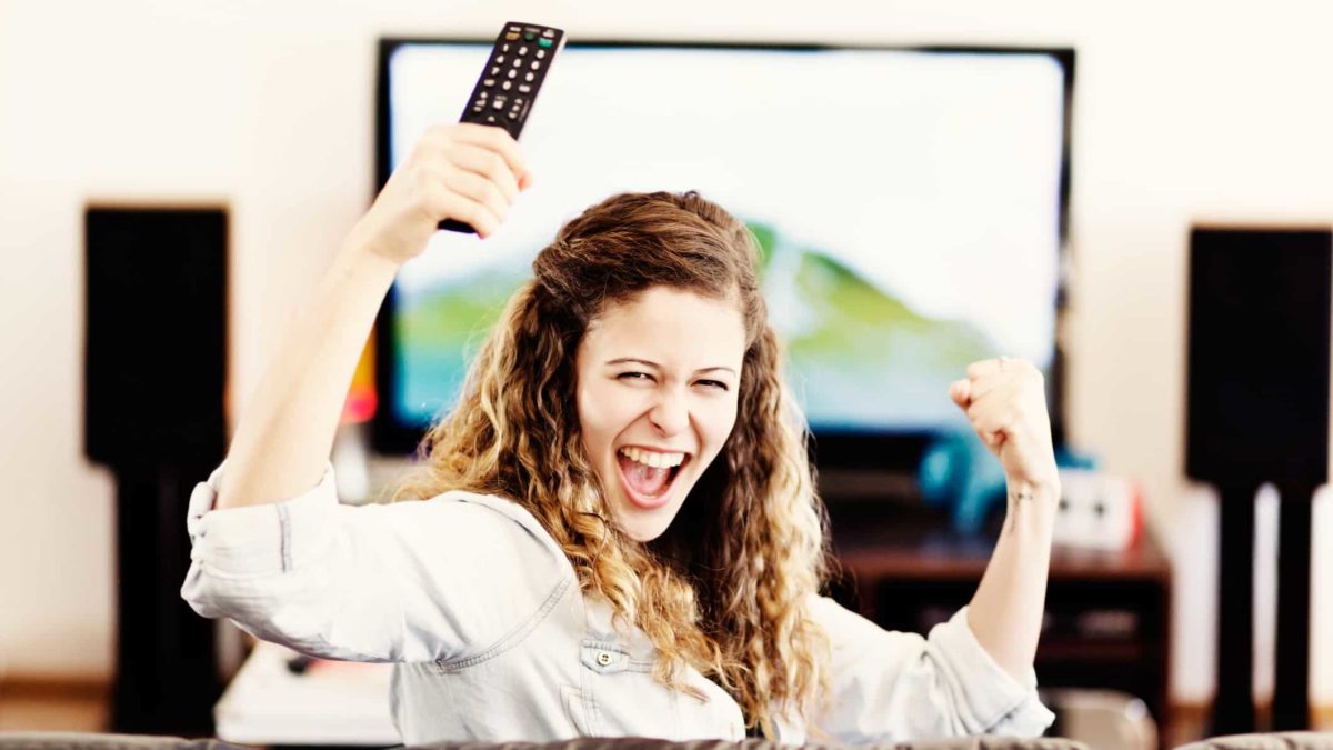 A woman looks back and cheers as she watches television.