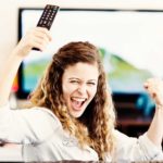 A woman looks back and cheers as she watches television.