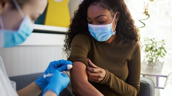 A nurse administers a vaccine into the arm of a woman wearing a mask.