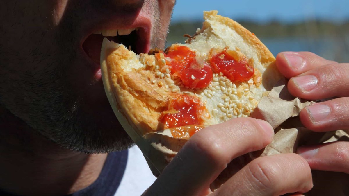A person eats a meat pie on the beach... what's more Australian than that?