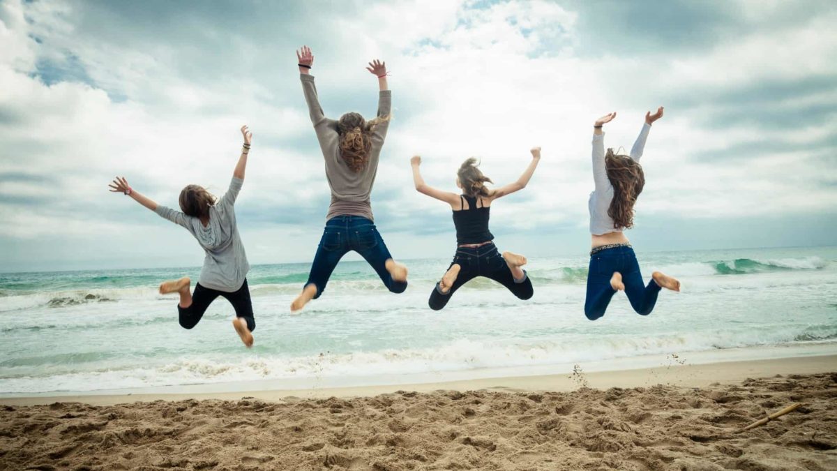 Four people on the beach leap high into the air.