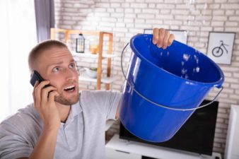 A man holds a bucket to stop the roof leaking while on the phone calling for help.