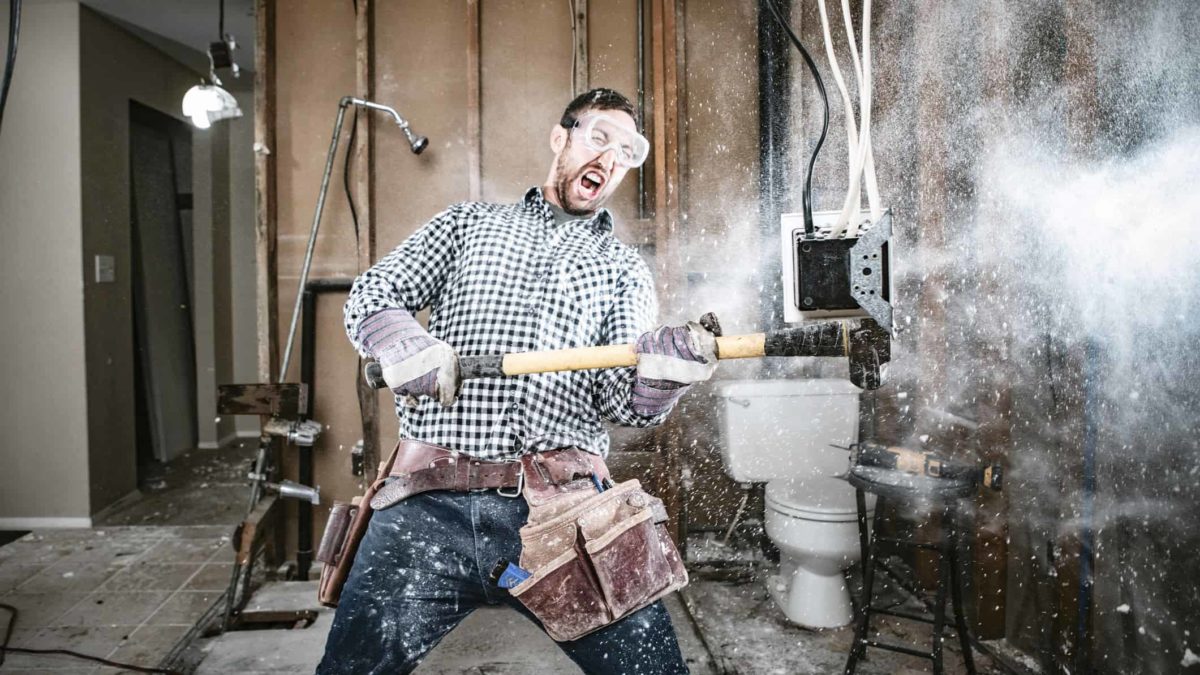 A man renovating his home wields a sledge hammer and with an almighty swing demolishes a wall.