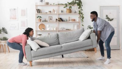 A guy helps a girl lift a couch, both are laughing.