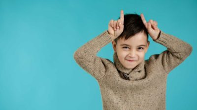 A little boy holds his fingers to his head posing as a bull.