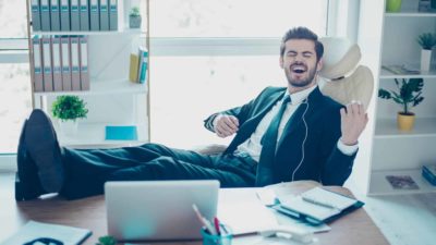 A man in a suit plays air guitar at his desk like a boss.