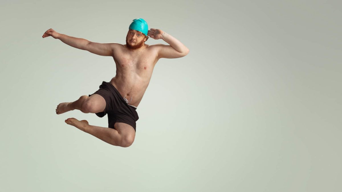 A man leaps through the air with a swimming cap and a look of uncertainty.